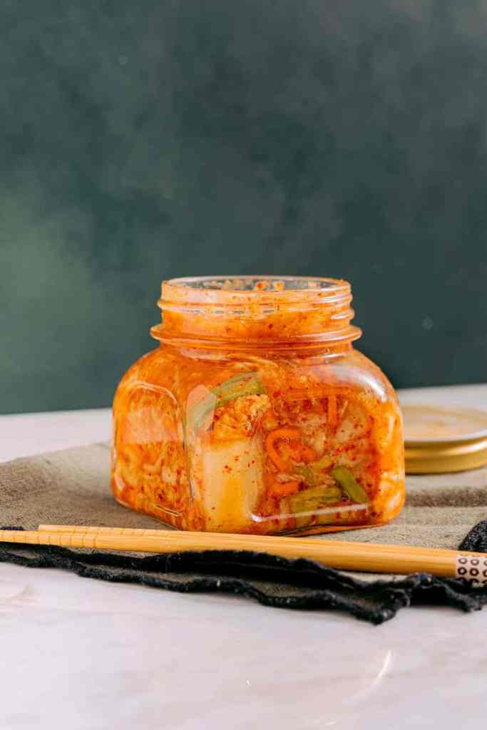 clear glass jar with kimchi beside the wooden chopsticks